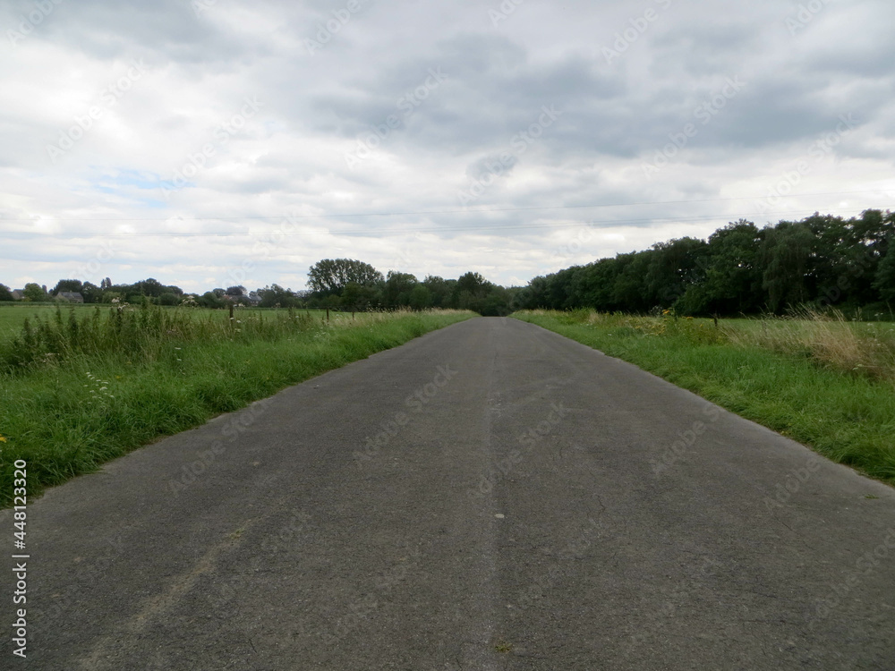 Longue route au milieu des prés sous un ciel nuageux