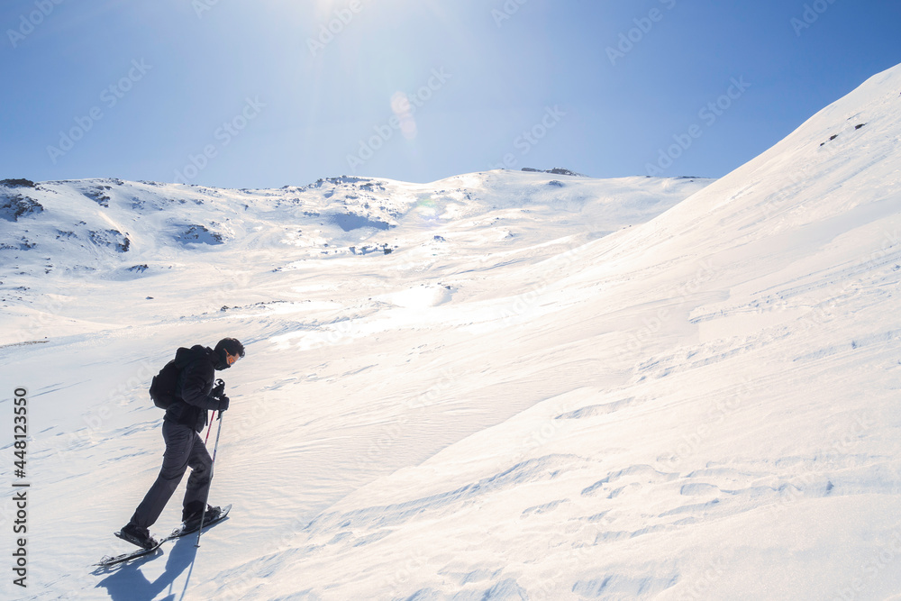 A man climbing the mountain through the snow.  with snowshoes and hiking sticks. Winter trip. 