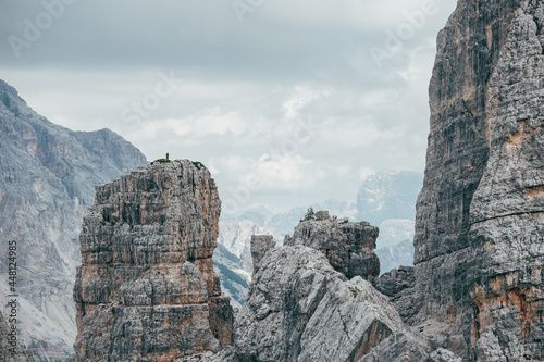 Small climber silhouette standing on impressive and picturesque Cinque Torri formation cliff who enjoying Dolomite Alps panorama. Extreme Active people and mountains concept.