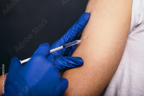 Man got a dose of the covid vaccine intramuscular. Nurse doctor vaccination a patient`s shoulder in hospital. Woman wear blue rubber sterile gloves hold syringe liquid solution medication drug

