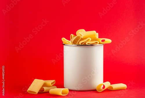 White kitchen jar mockup with cannelloni pasta on modern podium on red background with copy space. Horizontal imade of container with empty space for logo photo