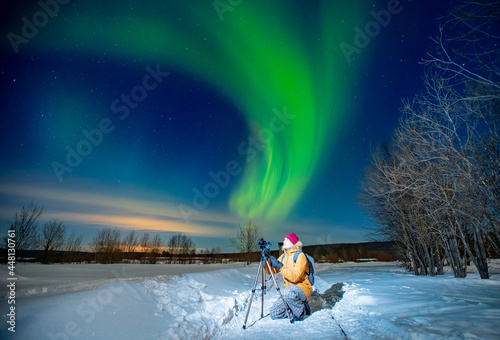 Photographer man with camera and tripod photographs aurora borealis, northern lights green. Concept photo tour to arctic travel