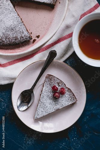 Chocolate cake decorated with cranberries and powdered sugar, kladdkaka with a cup of tea on a blue background.  Swedish desert. White dish towel. 