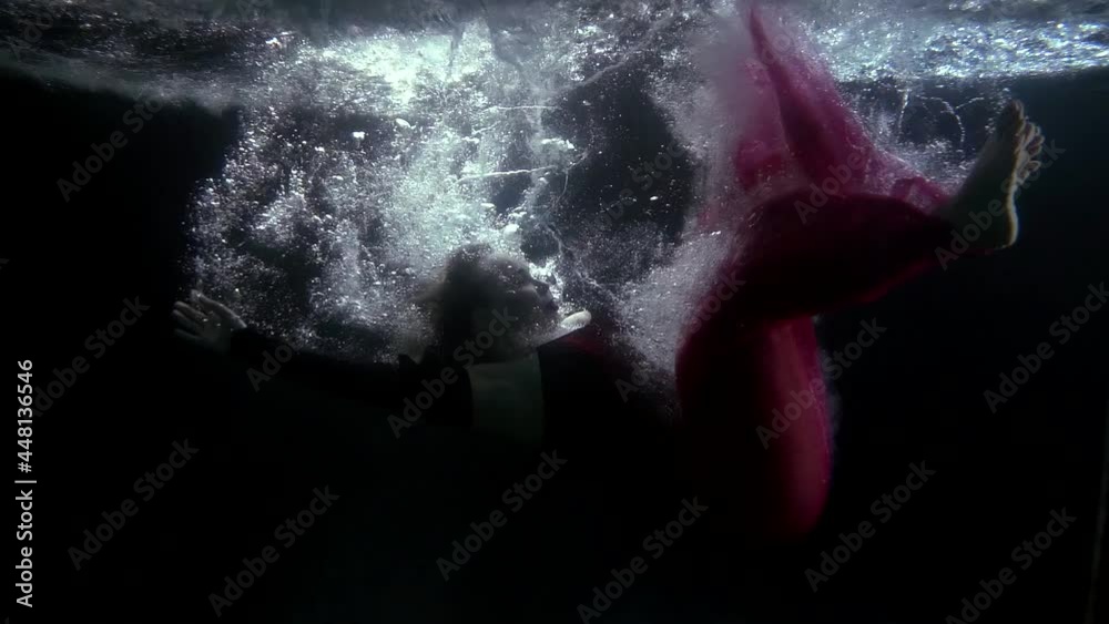 a blonde in a red dress falls into the dark water and swims in bubbles