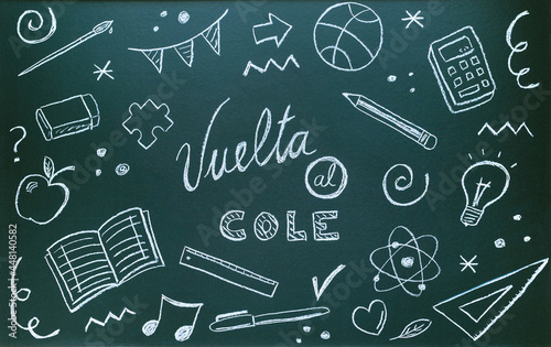 Blackboard written with chalk with spanish message and school supplies. Back to school concept photo