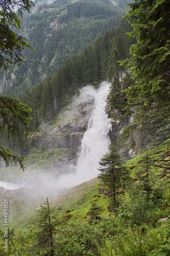 A waterfall in a green forest. Rocks. Fir trees. Mountain slope. Green grass.