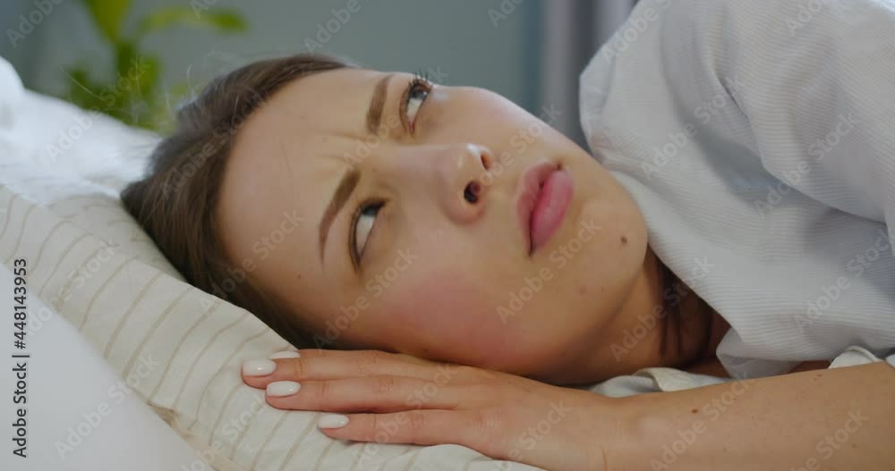 Close up of Caucasian beautiful unhappy young woman sleeping in bed and waking up from bad noise. Pretty female trying to sleep annoyed by noisy neighbors covering ears with pillow. Insomnia concept Close up of Caucasian beautiful unhappy young woman sleeping in bed and waking up from bad noise. Pretty female trying to sleep annoyed by noisy neighbors covering ears with pillow. Insomnia concept
