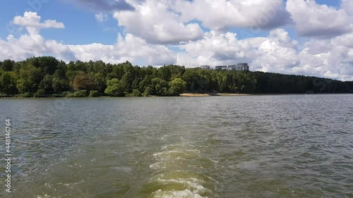 Motor boat trip along the waves of the picturesque Senezh lake. Skyline, green trees on the shore and cloudy blue sky on a sunny day. Moscow region, Russia