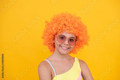 happy child in sunglasses and swimsuit wearing orange curly wig hair, summer fun.