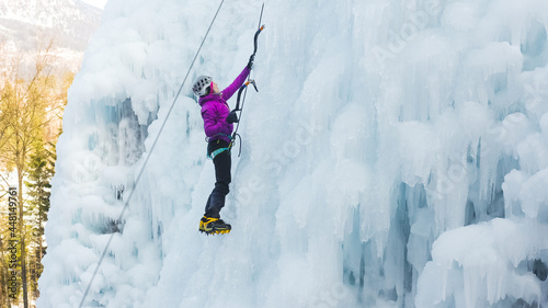 Female ice climber silhouette swinging ice axes on her way up vertical ice waterfall, side view