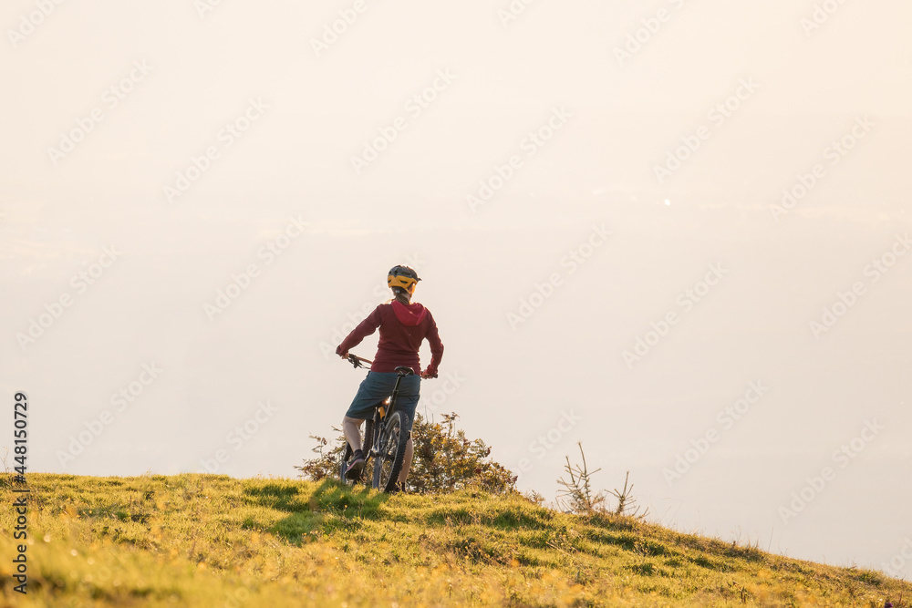 Woman on mountain bike looking at sunset in nature Woman on mountain bike looking at sunset in nature