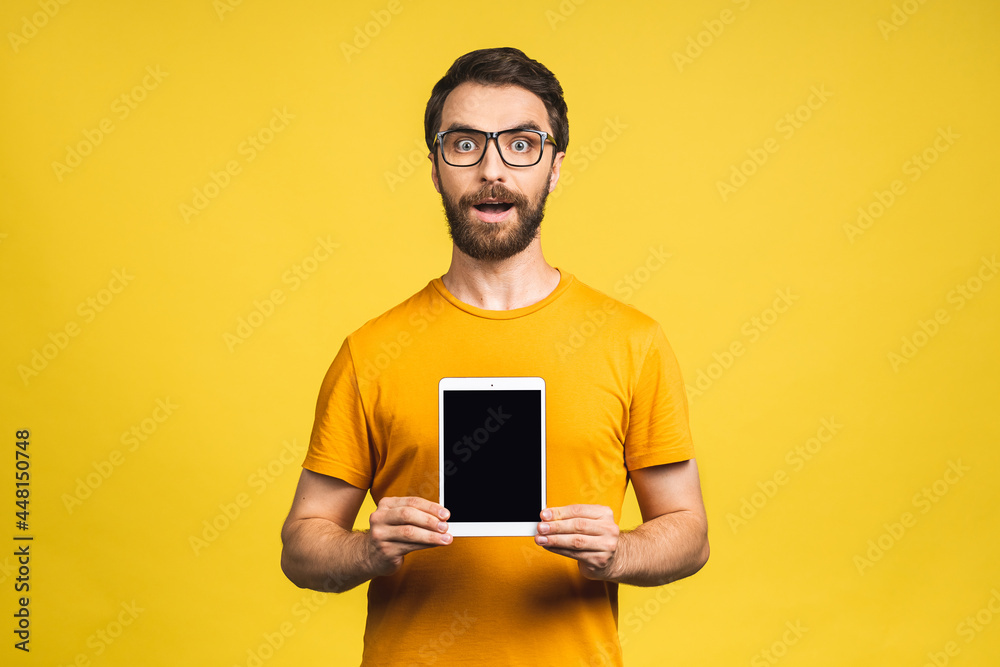 Product presentation. Promotion. Young bearded man holding in hands tablet computer with blank screen. Isolated over yellow background.