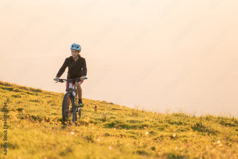 Fototapeta premium Girl child riding mountain bike into the sunset. Beautiful golden summer light.