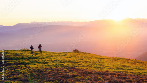 Mother and daughter cycling on mountain bikes at a sunset in mountains.