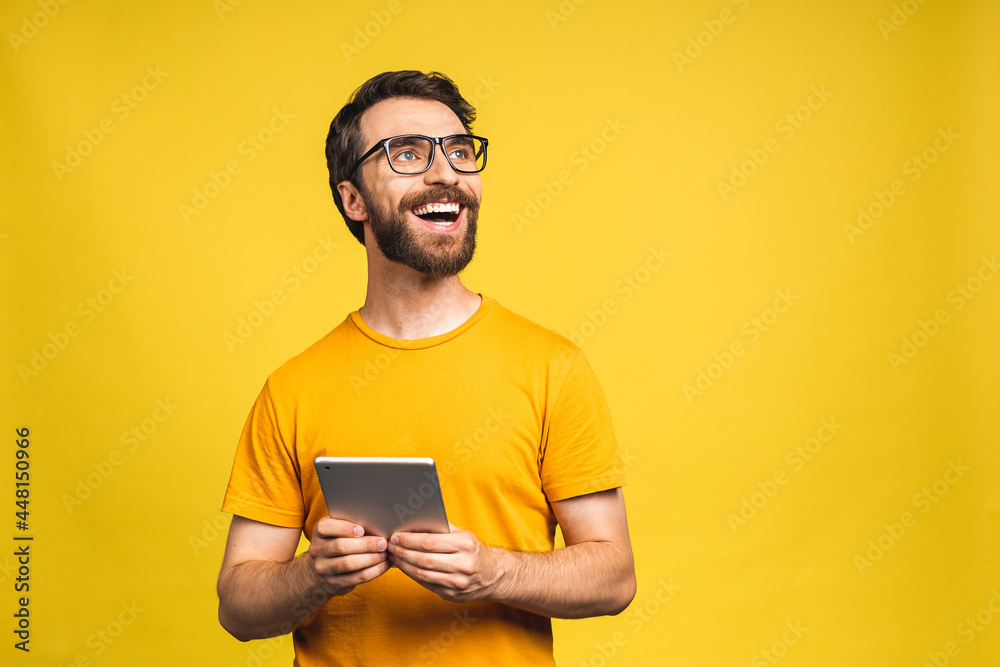 Happy young man in casual standing and using tablet computer isolated over yellow background. Happy young man in casual standing and using tablet computer isolated over yellow background.