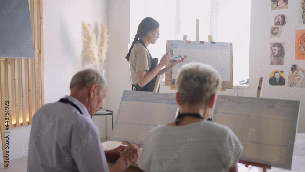 The teacher shows a group of friends of retired people in the elderly at drawing courses. A group of elderly men and women draw together and smile The teacher shows a group of friends of retired people in the elderly at drawing courses. A group of elderly men and women draw together and smile