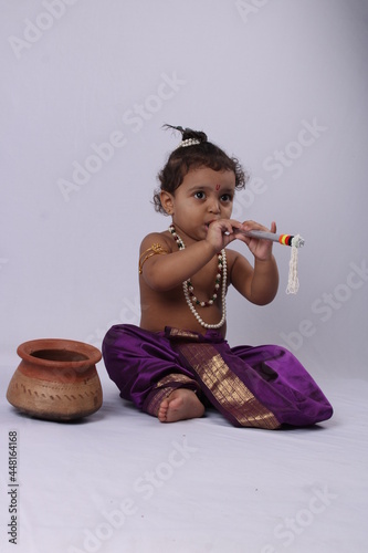 adorable Indian baby in krishna kanha or kanhaiya dress posing with his flute and peacock feather on white background. standing pose photo