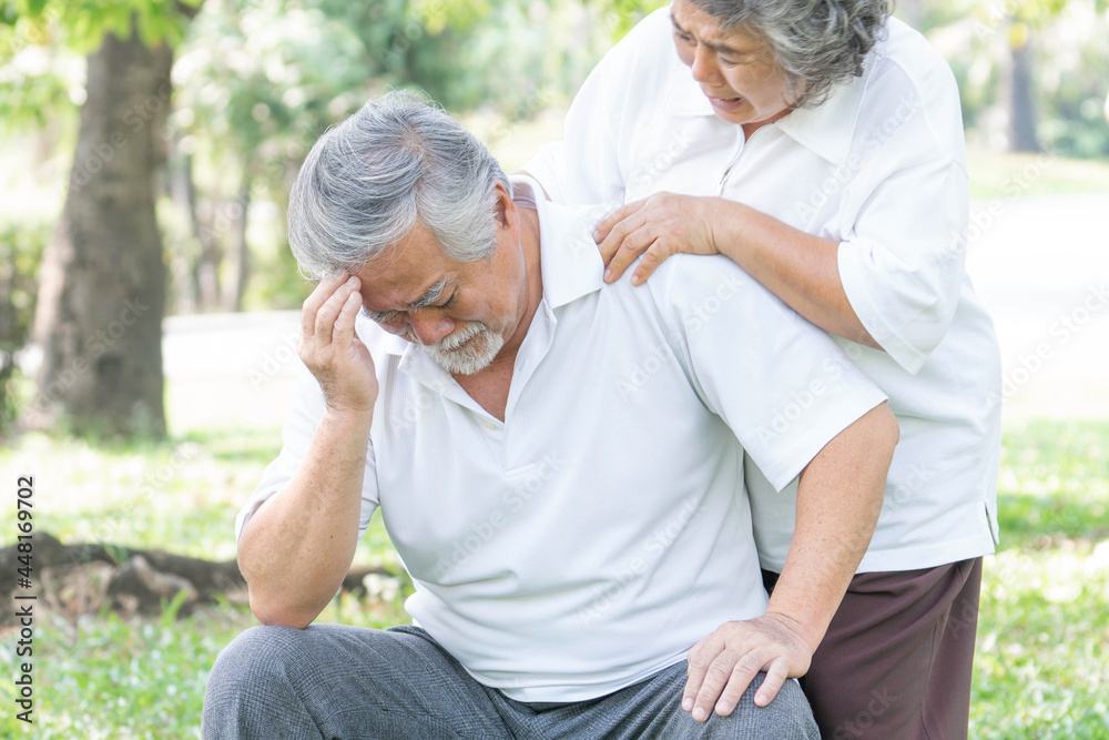 Senior male Asian suffering in a forest , headache high blood pressure at garden park , Wife supporting husband - Elderly Asian senior man patients headache hypertension concept Senior male Asian suffering in a forest , headache high blood pressure at garden park , Wife supporting husband - Elderly Asian senior man patients headache hypertension concept