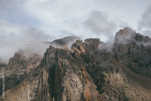 Scenic mountain landscape with great rocks in cloudy sky in vintage colors. Awesome sunny scenery with low clouds on rocky mountain top in pastel tones. Beautiful brown rock in sunlight and low clouds