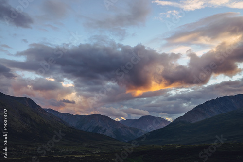Beautiful mountain scenery with golden dawn light in cloudy sky. Scenic mountain landscape with illuminating color in sunset sky. Silhouettes of mountains on sunrise. Gold illuminating sunlight in sky © Daniil