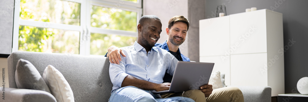 Gay Couple Using Computer For Video Conference On Sofa Gay Couple Using Computer For Video Conference On Sofa