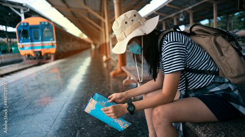 New normal traveler concepts. Young female tourist wearing a mask looks at a tourist map while waiting for a train at the train station.