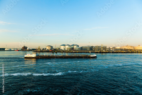 An oil refinery in Amsterdam by the water and a small river tanker passing by.