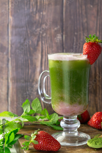 Strawberry Matcha latte in a glass on a wooden table and wooden background, garnished with strawberries and mint leaves