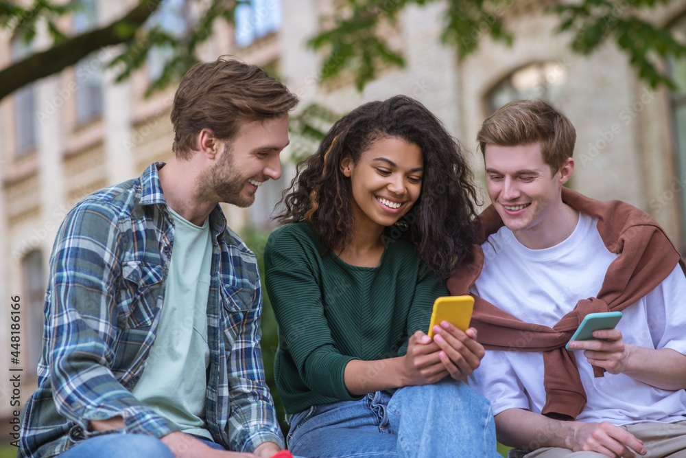 Fototapeta premium Group of young people sitting on the behcn and holding smartphones in hands