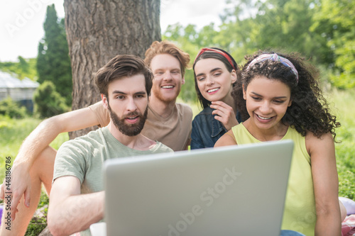 Four young happy friends looking at laptop