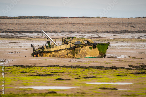 A damaged boat in the mud of the Walney Channel, seen from the road to Roa Island, Cumbria, England, UK