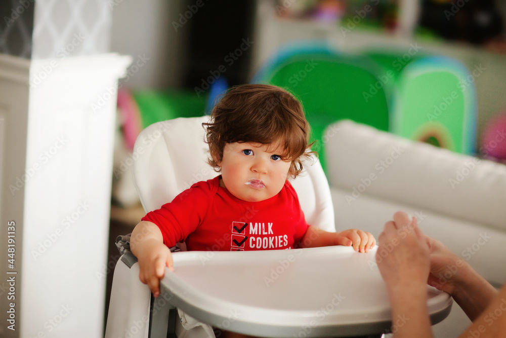 Curly little boy in a red bodysuit sits with a high chair Curly little boy in a red bodysuit sits with a high chair