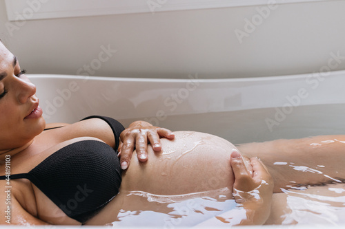 Pregnant woman in bathtub admiring belly bump