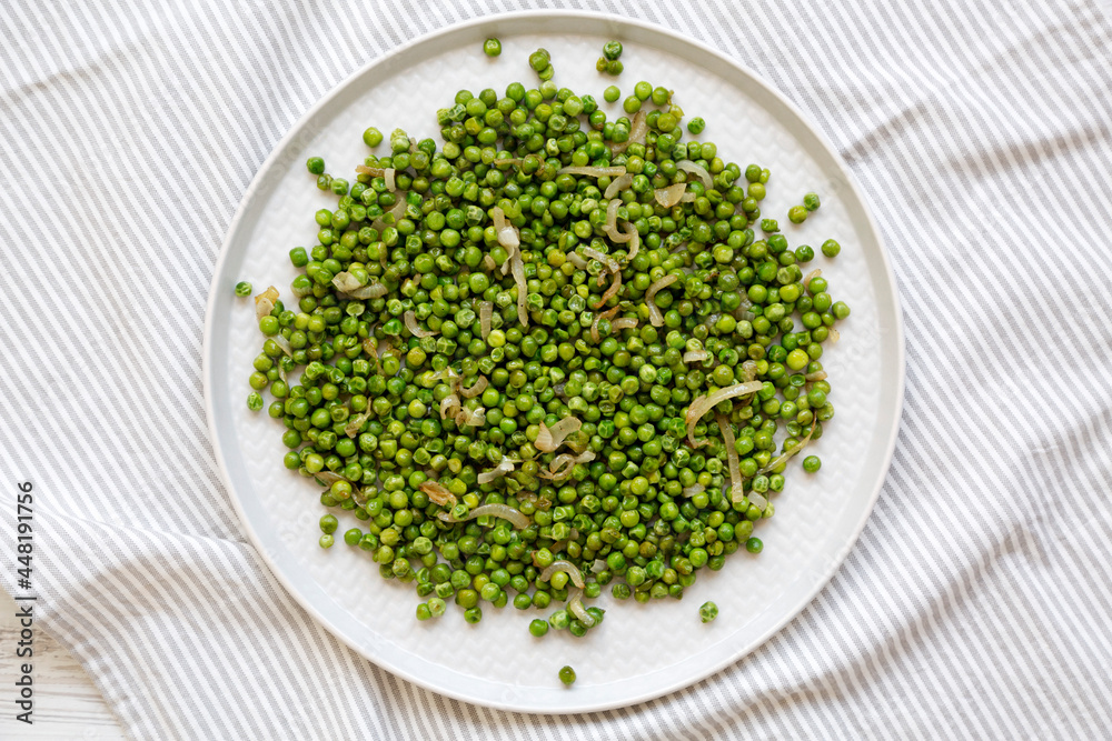 Homemade Sauteed Green Peas on a plate on a white wooden background, top view. Flat lay, overhead, from above. Homemade Sauteed Green Peas on a plate on a white wooden background, top view. Flat lay, overhead, from above.
