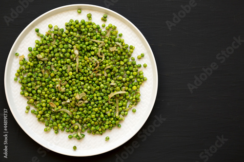 Homemade Sauteed Green Peas on a plate on a black background, top view. Flat lay, overhead, from above. Copy space.