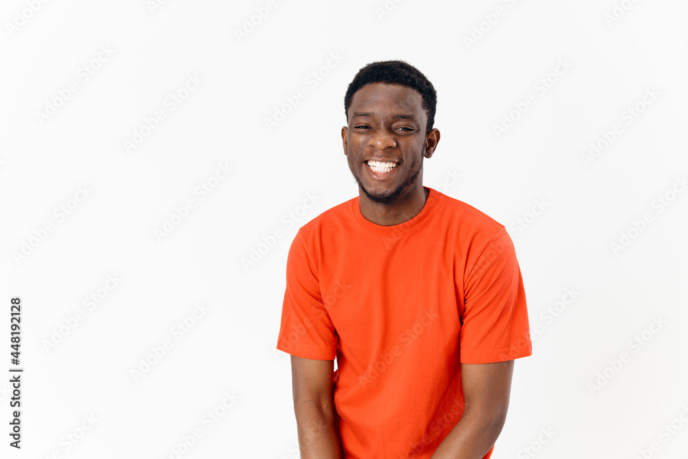 happy african american guy in an orange t-shirt on a light background laughs front view happy african american guy in an orange t-shirt on a light background laughs front view