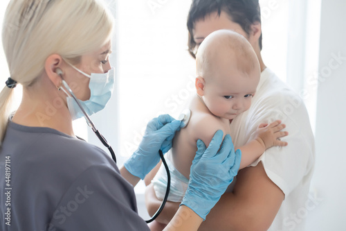Female doctor examining little smiling baby girl, held by mother