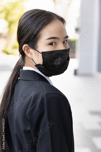 Compliant vaccinated asian office worker or businesswoman wearing face mask and looking back, concept of mask mandate and social distancing again regardless of vaccination status