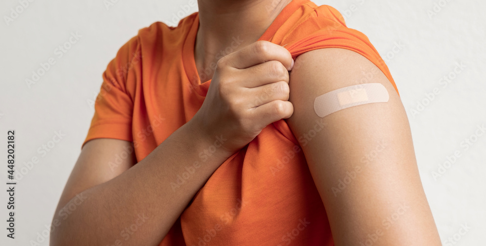 Asian woman shows plaster on her shoulder after being vaccinated against Covid-19. Coronavirus vaccination campaign concept - obrazy, fototapety, plakaty 