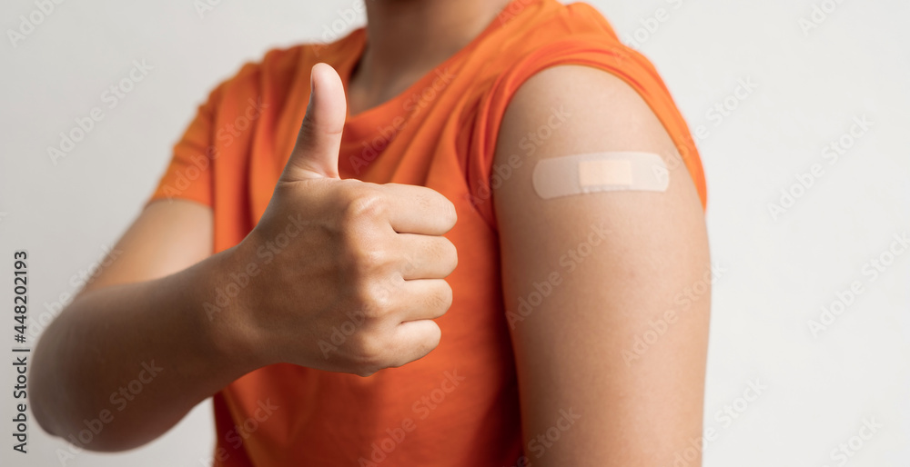 Asian woman shows plaster on her shoulder after being vaccinated against Covid-19. Coronavirus vaccination campaign concept - obrazy, fototapety, plakaty 