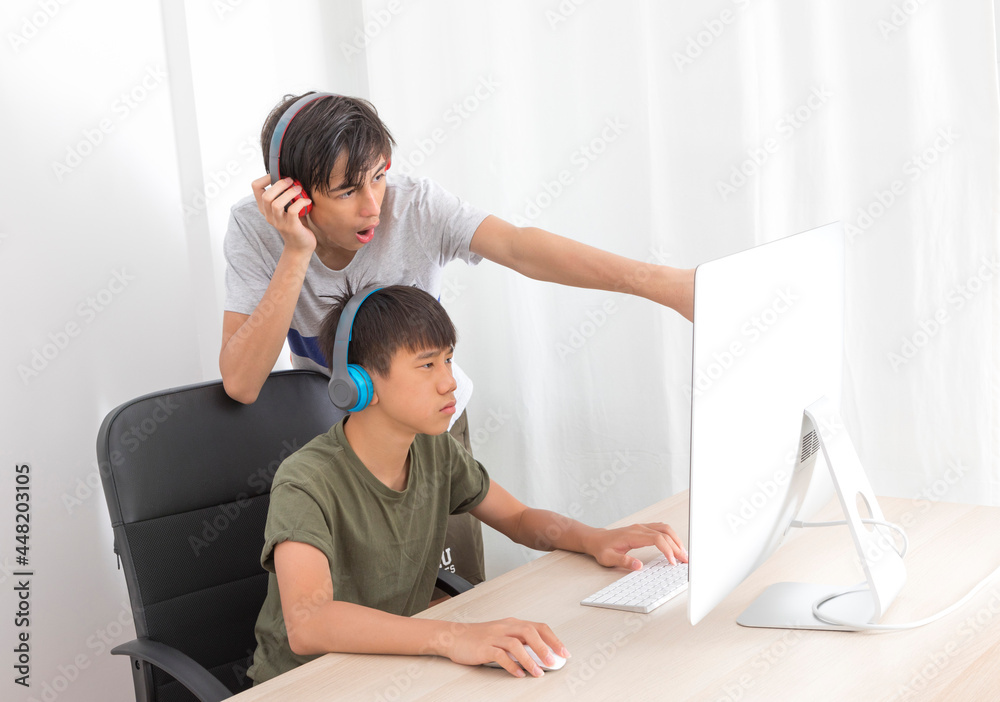 Two multiethnic teenage boys with headphone have fun with computer games at home.
