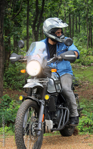 A young guy in a helmet is riding on a forest road on an electric motorcycle. He sits confidently in the saddle. There are green trees around him.