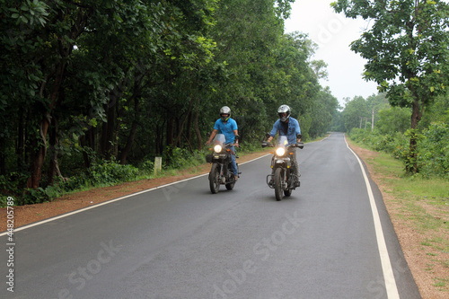 Two motorcyclists riding fast on their motorbikes through autumn forest. Friends having active rest in nature driving powerful motorcycles. Bikers enjoying trip together. Extreme sport concept.