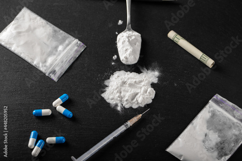 Cocaine and other drugs on a black background, close-up. A rolled up dollar bill for drug use.