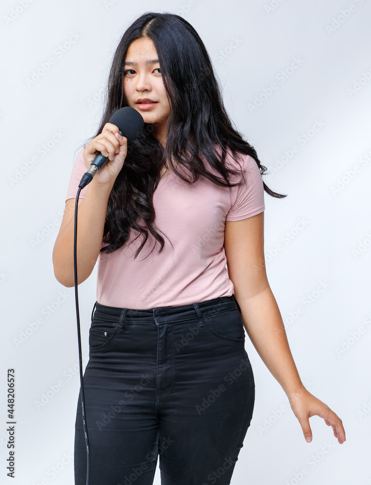 Portrait shot of young teenage singer singing a song with a microphone while looking at the camera. Junior student vocalist practicing isolated with white background. Concept of rehearsal and training Portrait shot of young teenage singer singing a song with a microphone while looking at the camera. Junior student vocalist practicing isolated with white background. Concept of rehearsal and training