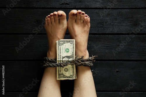 tying a leg with an old rope of a young girl and American dollars on nohs on the black floor, human trafficking, slavery ransom photo