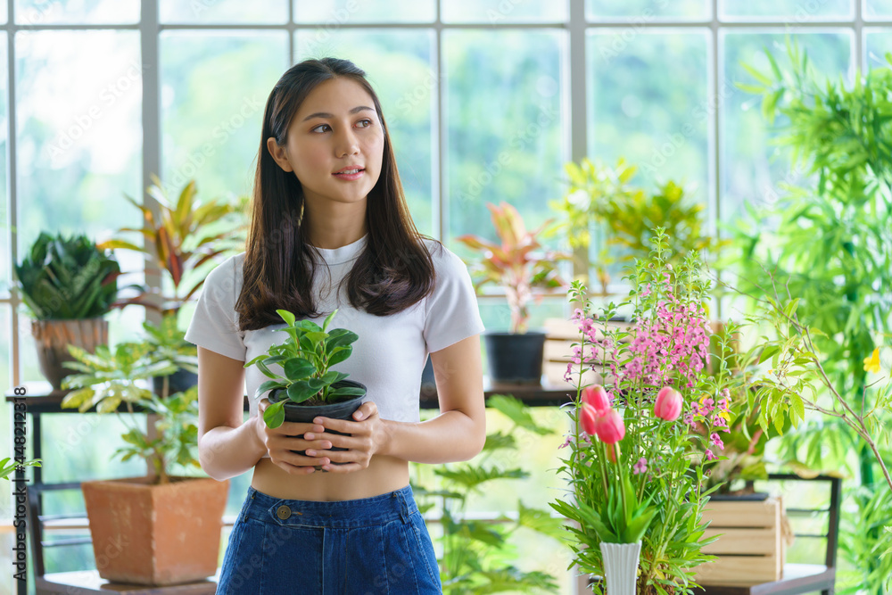 Joyful female entrepreneur florist plant seller holding a croton foliage plant pot in a floral shop Joyful female entrepreneur florist plant seller holding a croton foliage plant pot in a floral shop