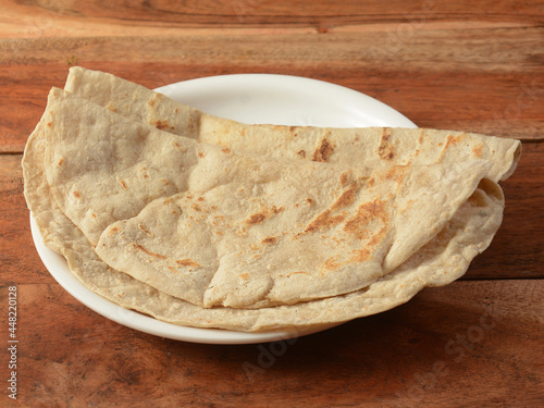 Bajra Roti or Bajra bhakri is a traditional Indian flat bread made with bajra or black pearl millet flour, served over a rustic wooden table, selective focus photo