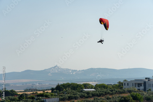 Side view of a powered Parachute. Ultralight Paramotor vehicle flying in the sky with green and mountains behind