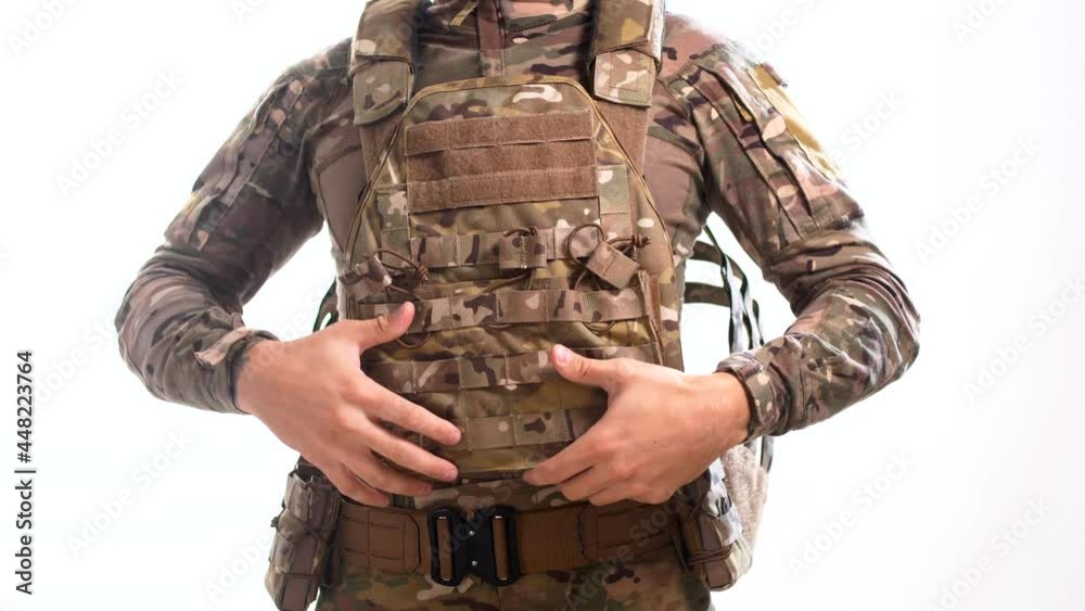 Man in combat camouflage is wearing a bulletproof vest over his head against a white background. Isolated Man in combat camouflage is wearing a bulletproof vest over his head against a white background. Isolated